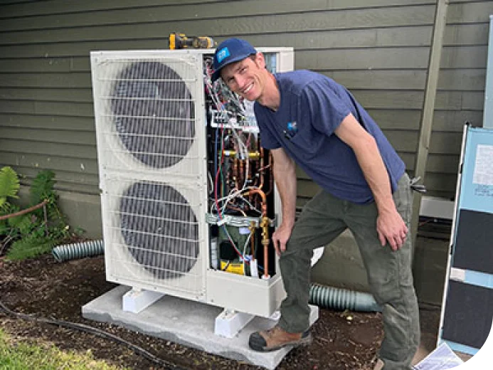 A College Place Heating & Air technician servicing an open heat pump unit outside a valley home